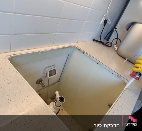 אדם עם כפפות צהובות מחזיק אקדח סיליקון ליד כיור פתוח